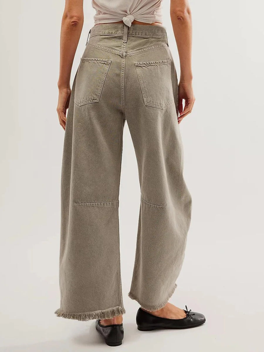 Back view of high-waisted, wide-leg taupe denim pants with frayed hems on a model.