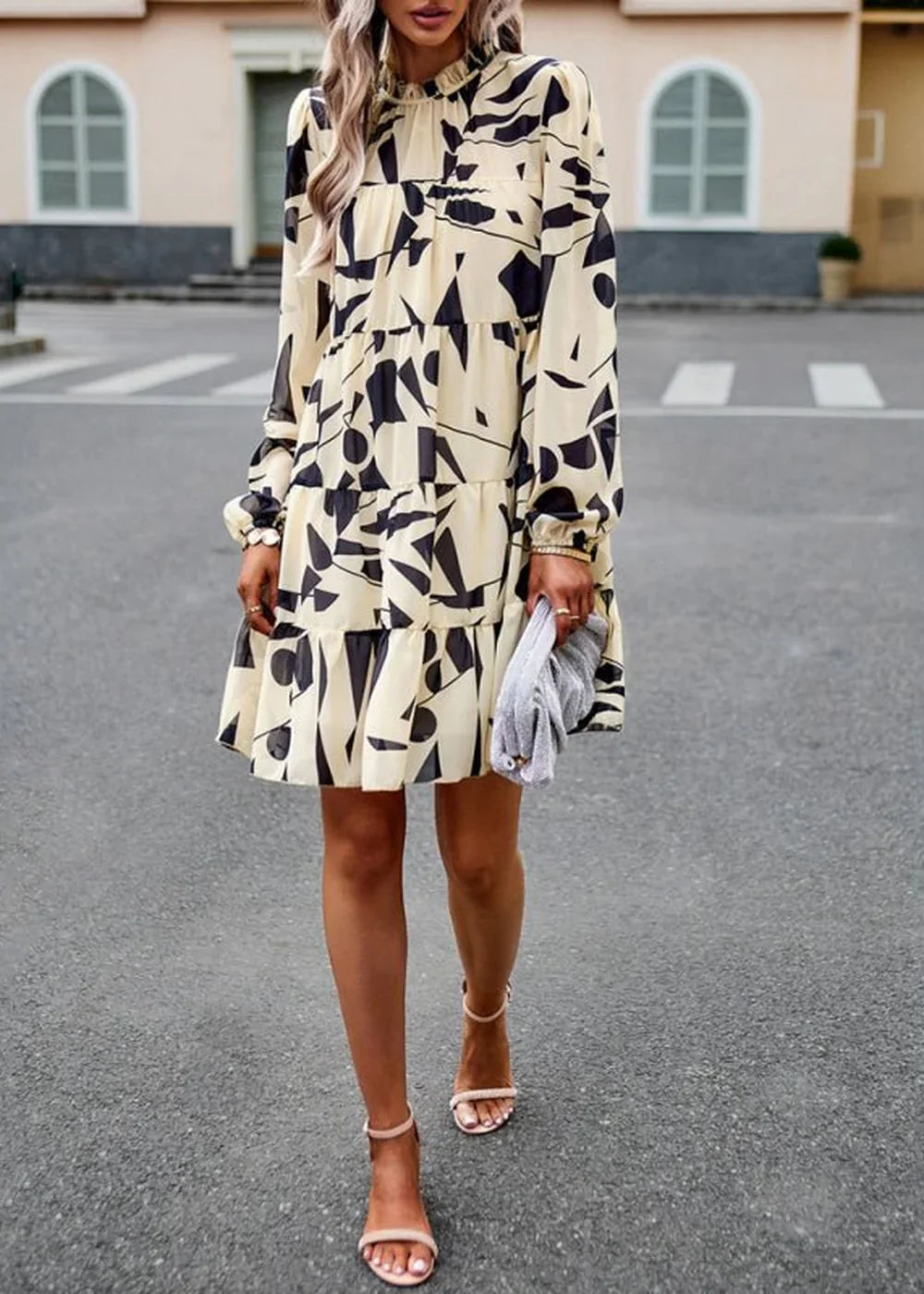 Cream and black abstract print tiered mini dress with long sleeves and ankle strap heels.