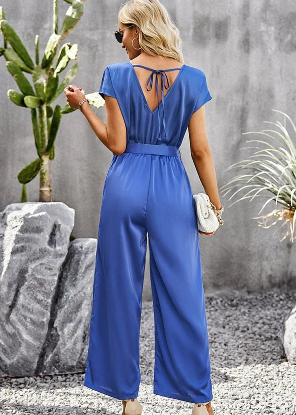 Back view of a woman wearing a royal blue wide-leg jumpsuit with a V-neck and tie detail.