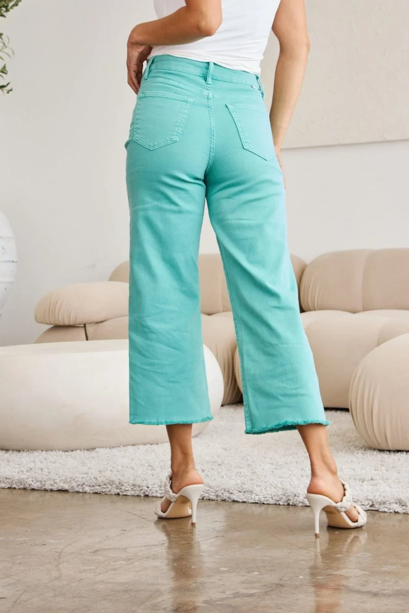 Turquoise cropped jeans with a frayed hem and moderate stretch, shown from the back on a model.