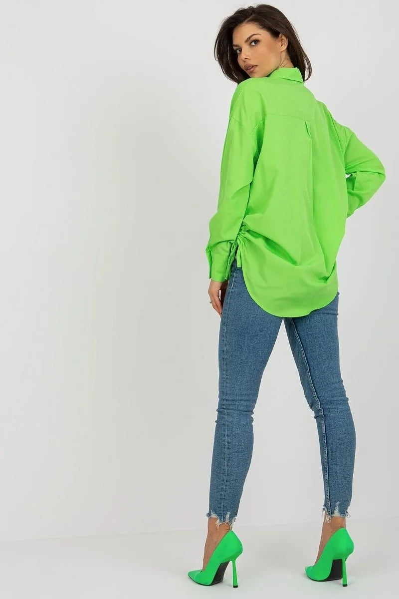 Lime green oversized button-up shirt with cinched sides, paired with distressed denim jeans and matching heels.