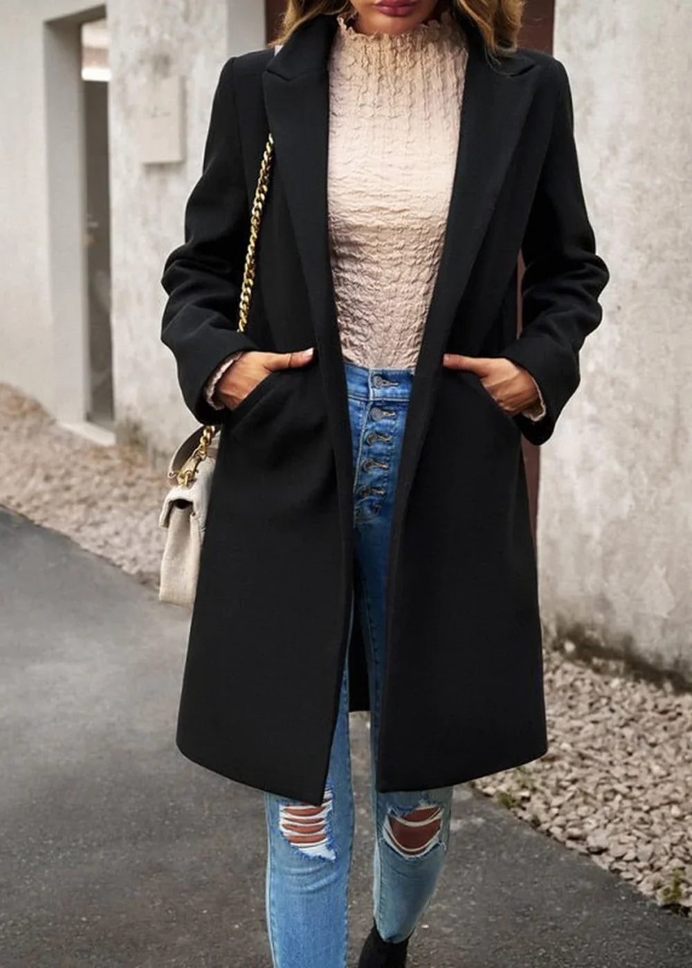 Black longline blazer with textured cream top, distressed blue jeans, and a cream crossbody bag.