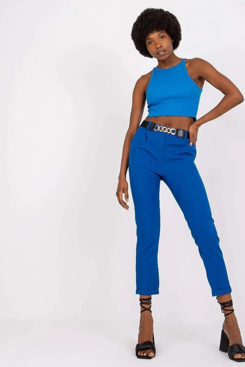Model in vibrant blue high-waisted pants with a black chain belt and black lace-up heels.