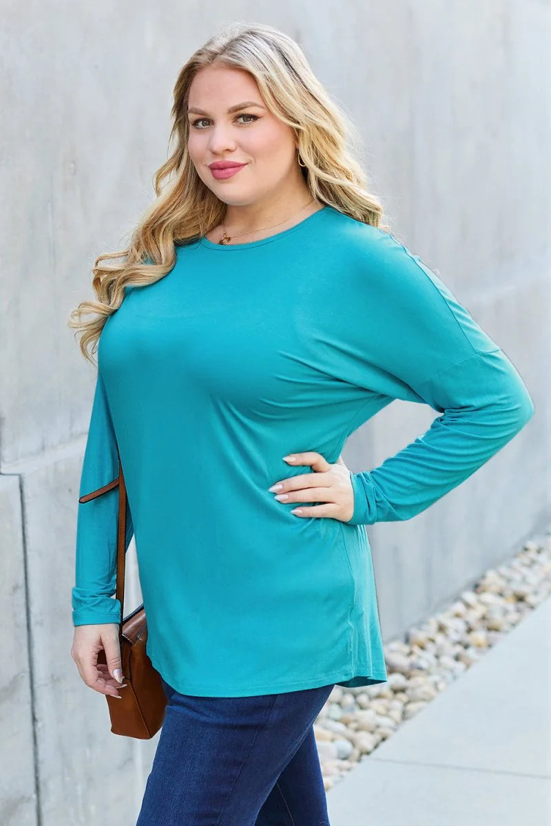 Teal long-sleeve top with relaxed fit, worn by a model with dark jeans and a brown crossbody bag.