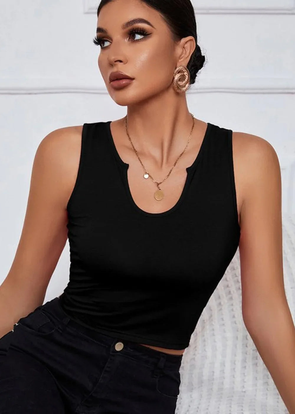 Black sleeveless crop top with a V-neck detail and gold pendant necklace on a model.