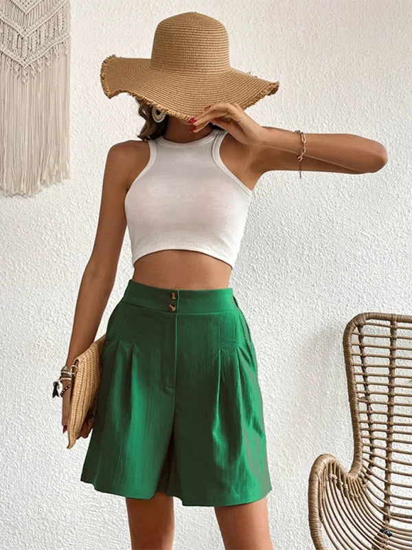 Woman wearing green linen-blend shorts with pleats and two buttons, holding a straw clutch.