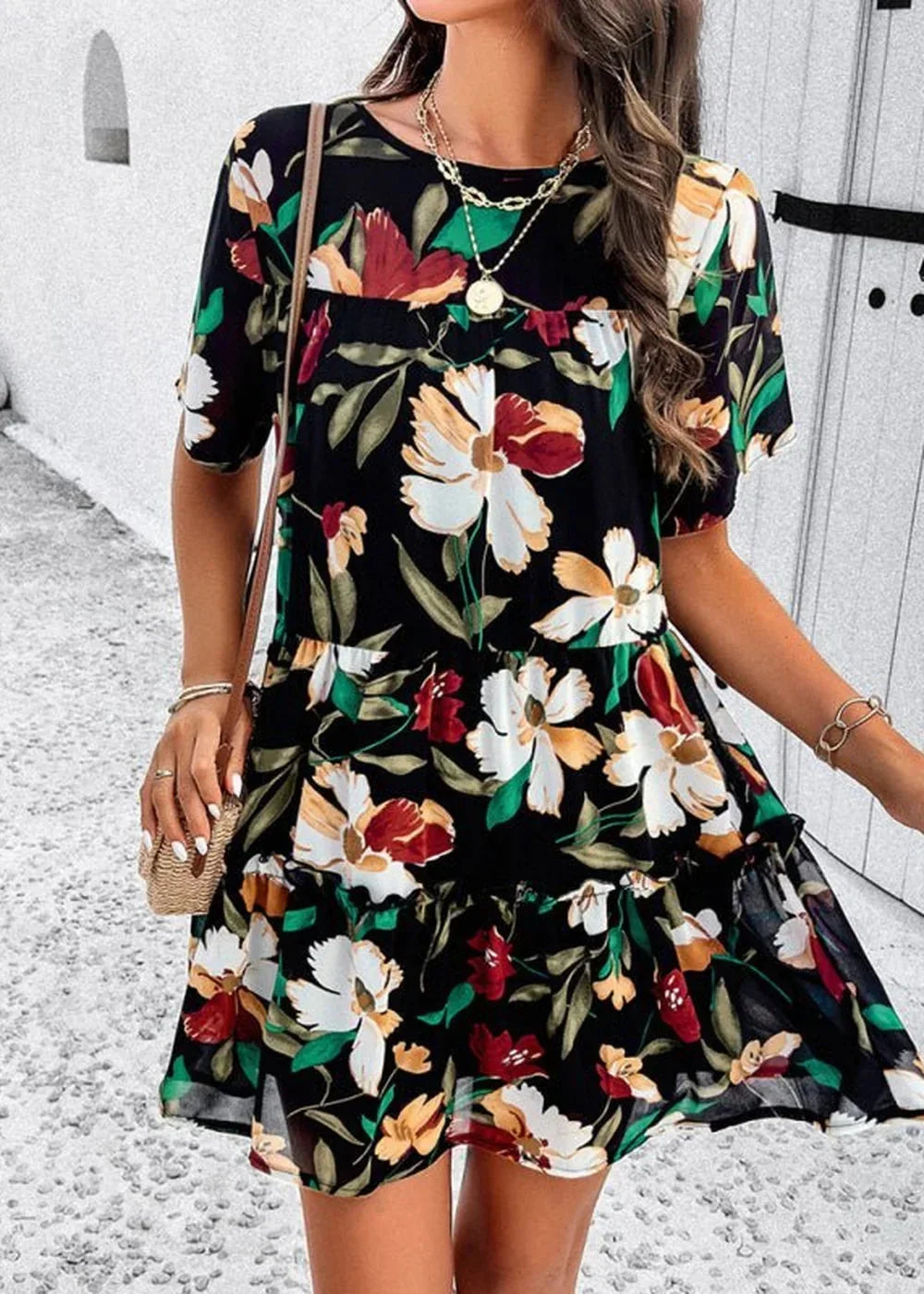 Black floral print dress with ruffles, gold necklaces, and a straw crossbody bag.