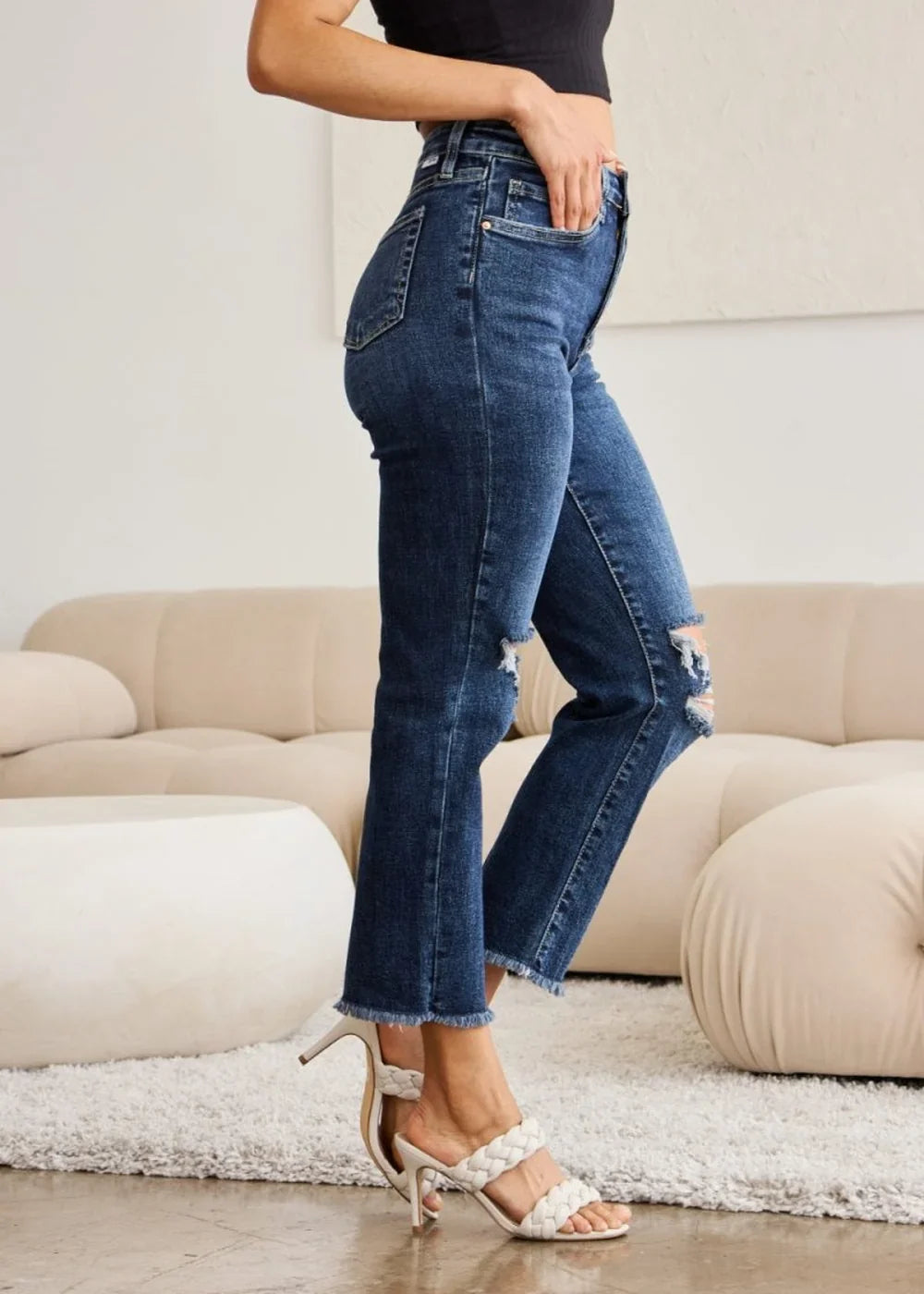 Distressed dark wash denim jeans with a frayed hem and cropped flare leg, worn by a model.