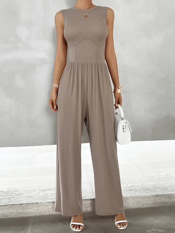 Taupe sleeveless jumpsuit with a fitted bodice, wide-leg pants, and a white handbag.
