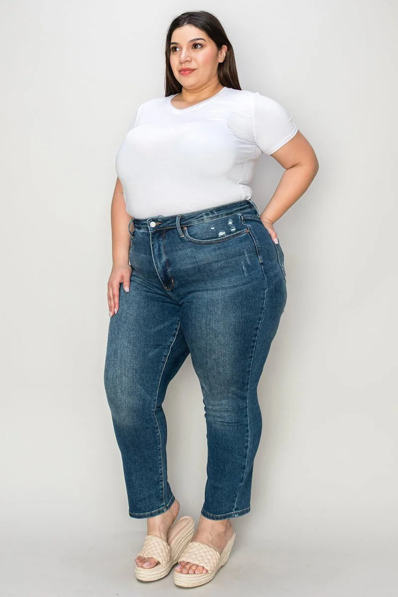 Plus-size model in distressed blue denim jeans and a white V-neck t-shirt, wearing cream wedge sandals.