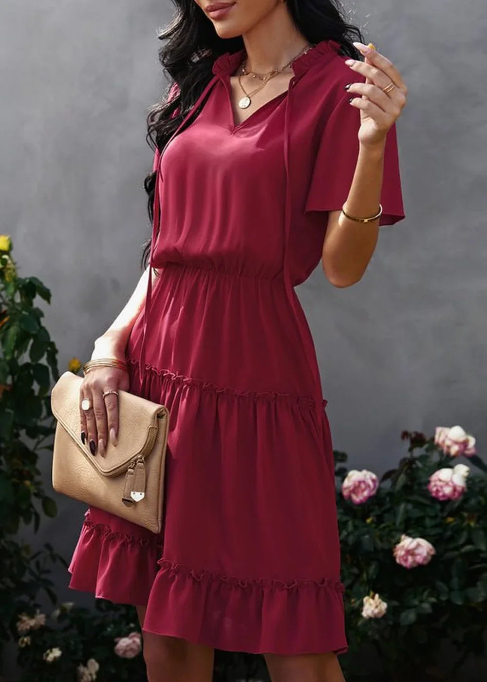 Woman in a ruffled, wine-red polyester dress with a tie-neck and a clutch.