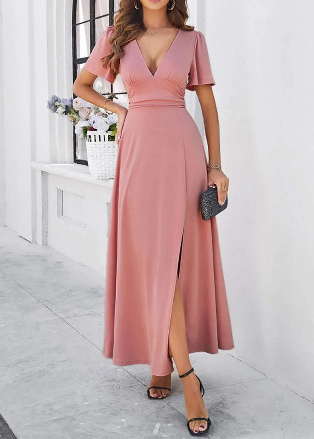 Pink v-neck maxi dress with flutter sleeves and a high slit, held by a model.