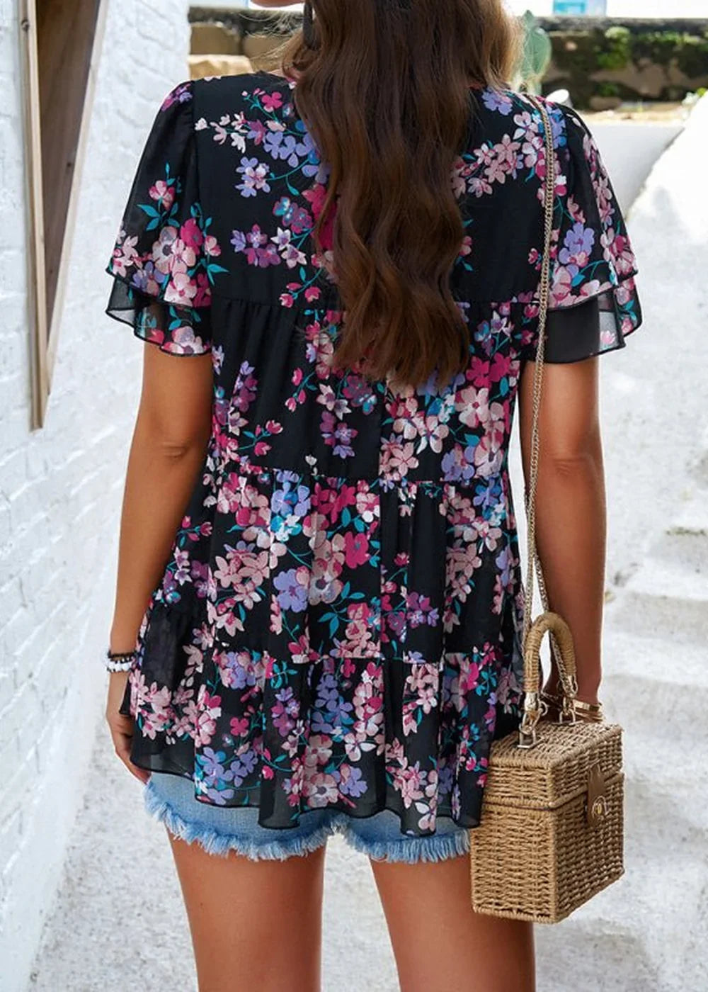 Black chiffon top with a colorful floral print, tiered ruffled sleeves, and a frayed denim hem.