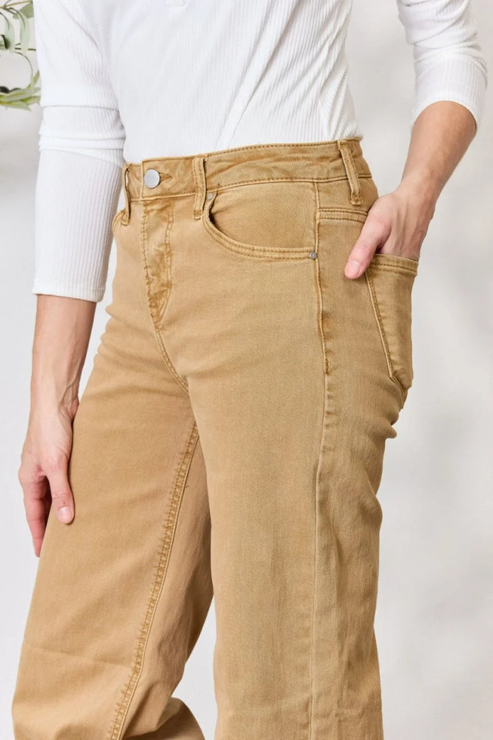 Close-up of tan denim jeans with a button closure and pockets on a model.