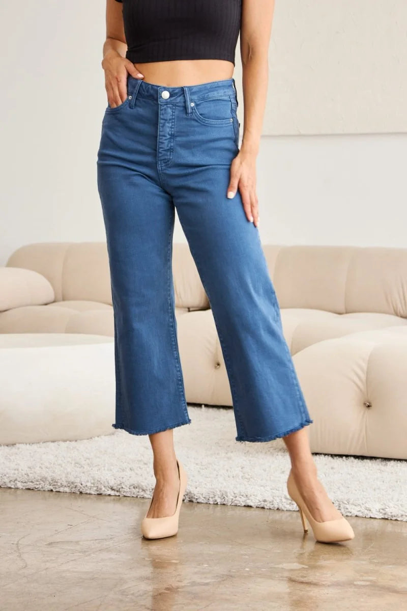 Blue denim crop flare jeans with a frayed hem, worn by a model on a couch.
