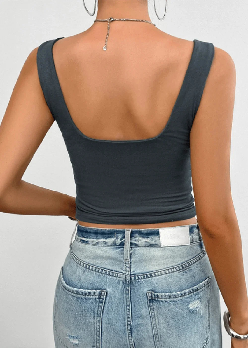 Back view of a woman wearing a slim-fit, dark grey scoop-neck tank top and light wash distressed denim jeans.