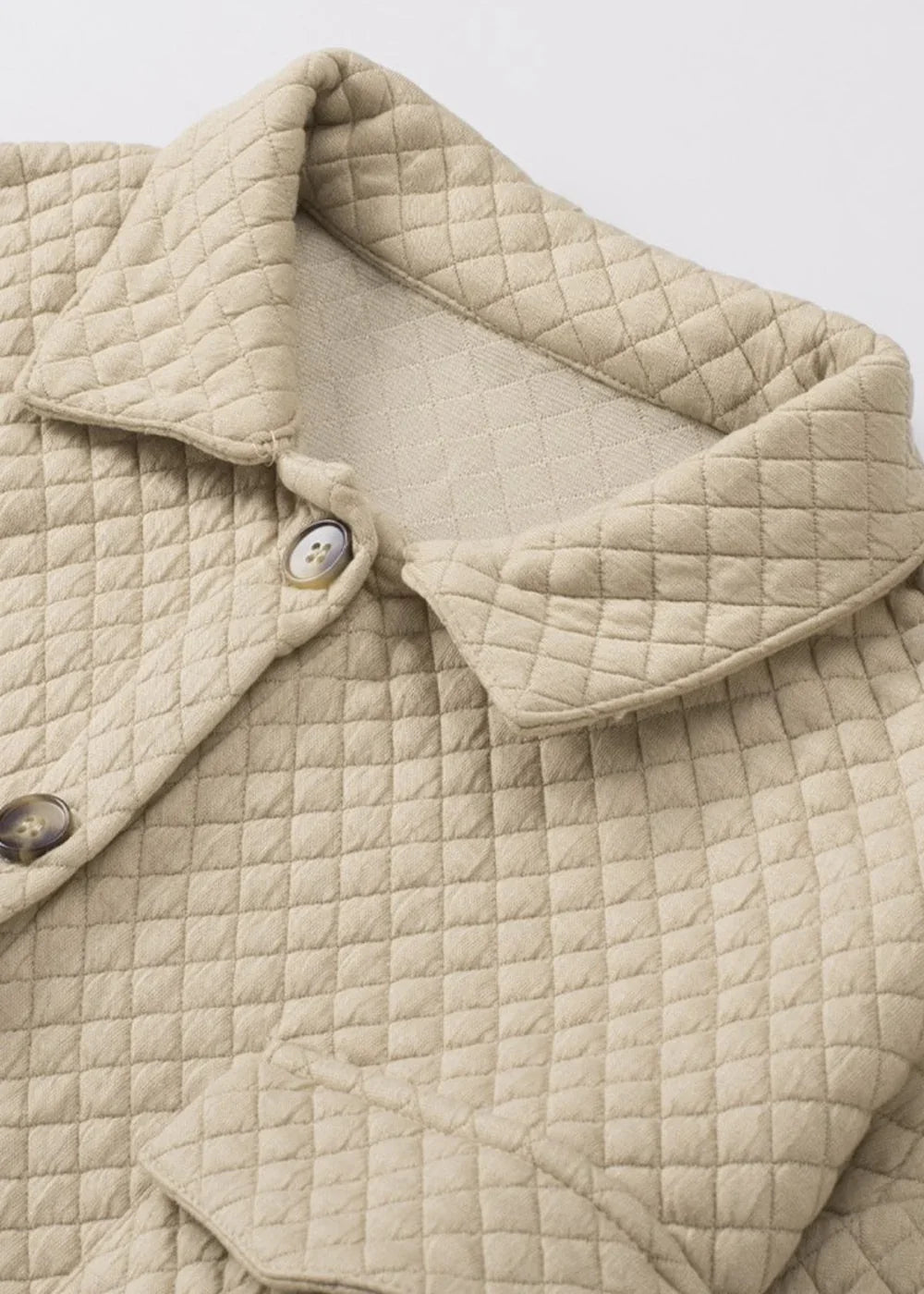Close-up of a beige quilted jacket collar and buttons, showing diamond pattern texture.