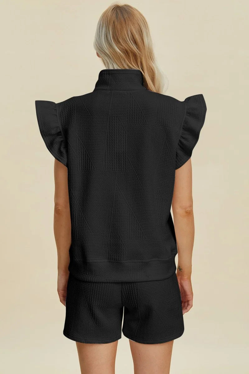 Black textured sleeveless top with ruffled shoulders and matching shorts on a model.