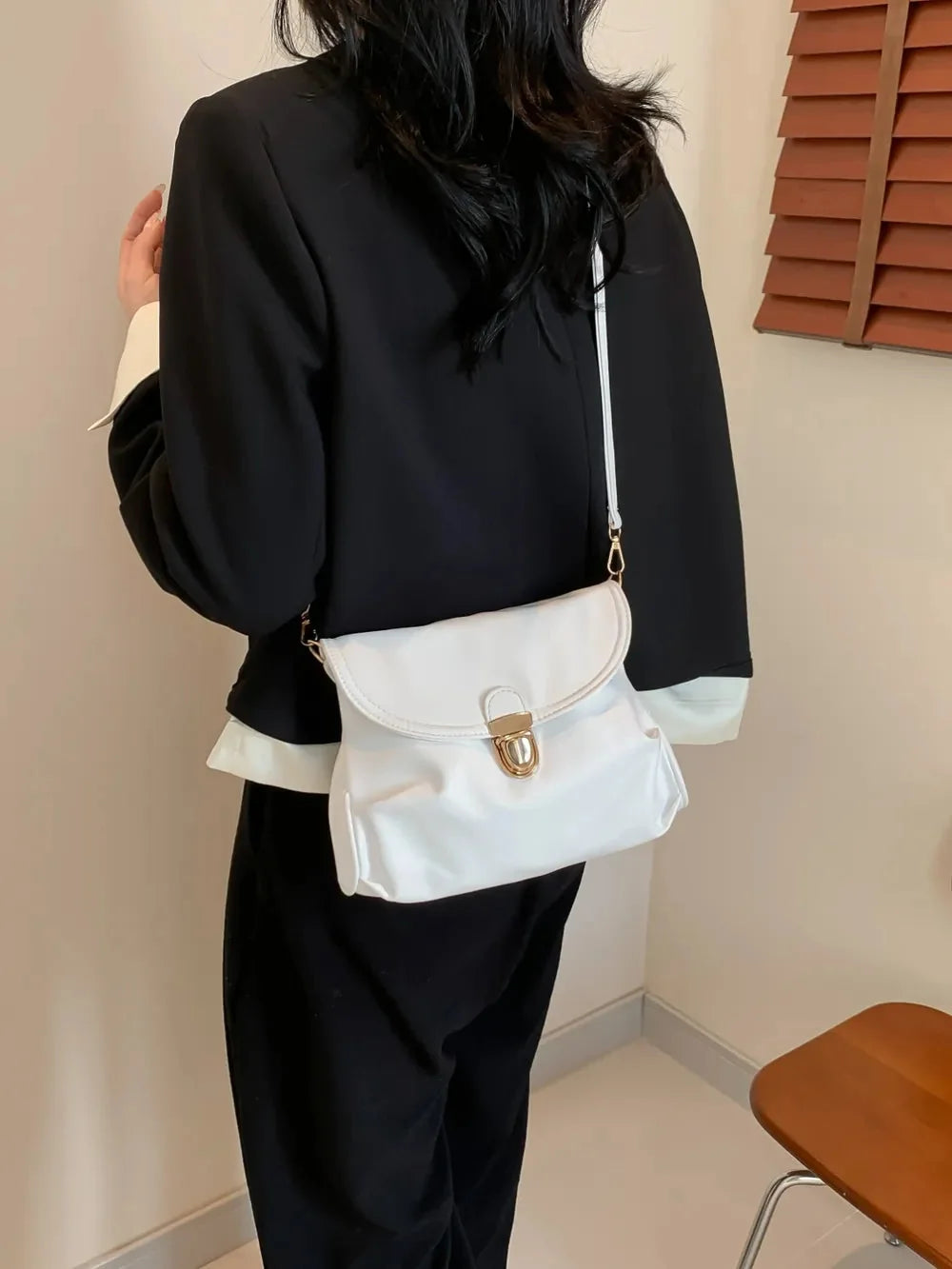 Woman in black blazer with white collar and cuffs, wearing a white crossbody bag with gold clasp.