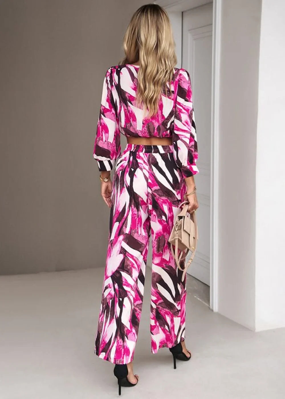 Back view of a woman wearing a pink, white, and black abstract print crop top and wide-leg pants.