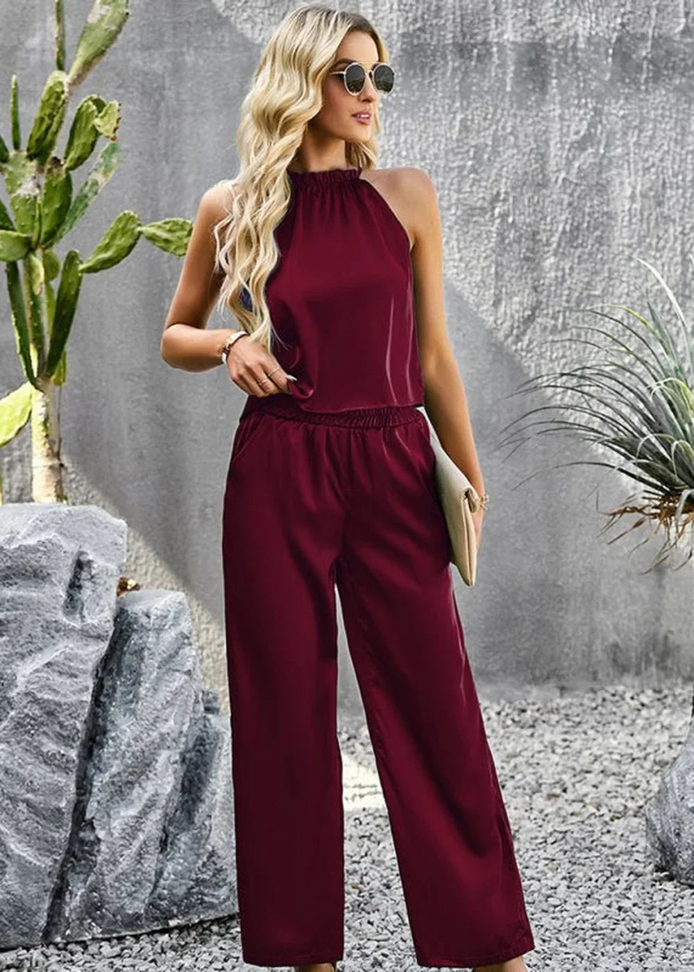 Burgundy halter neck jumpsuit with wide legs, elastic waist, and cream clutch.