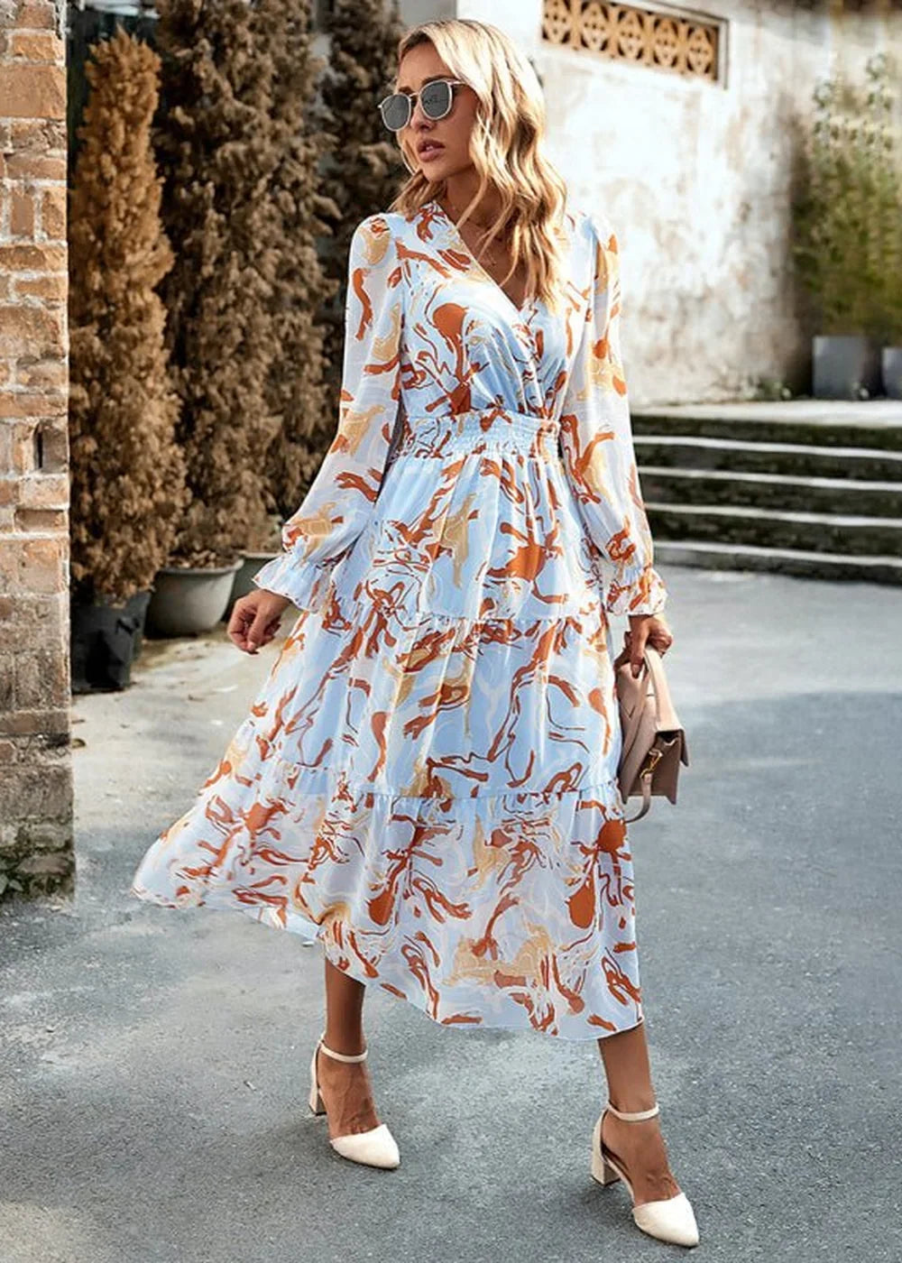 Light blue midi dress with orange abstract print, ruffled tiers, and v-neck on model.