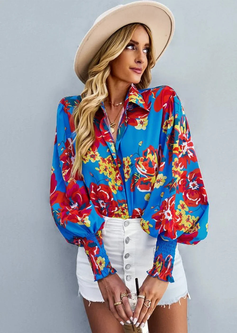 Woman in a vibrant floral print blouse with balloon sleeves and a white button-front mini skirt, wearing a wide-brimmed hat.