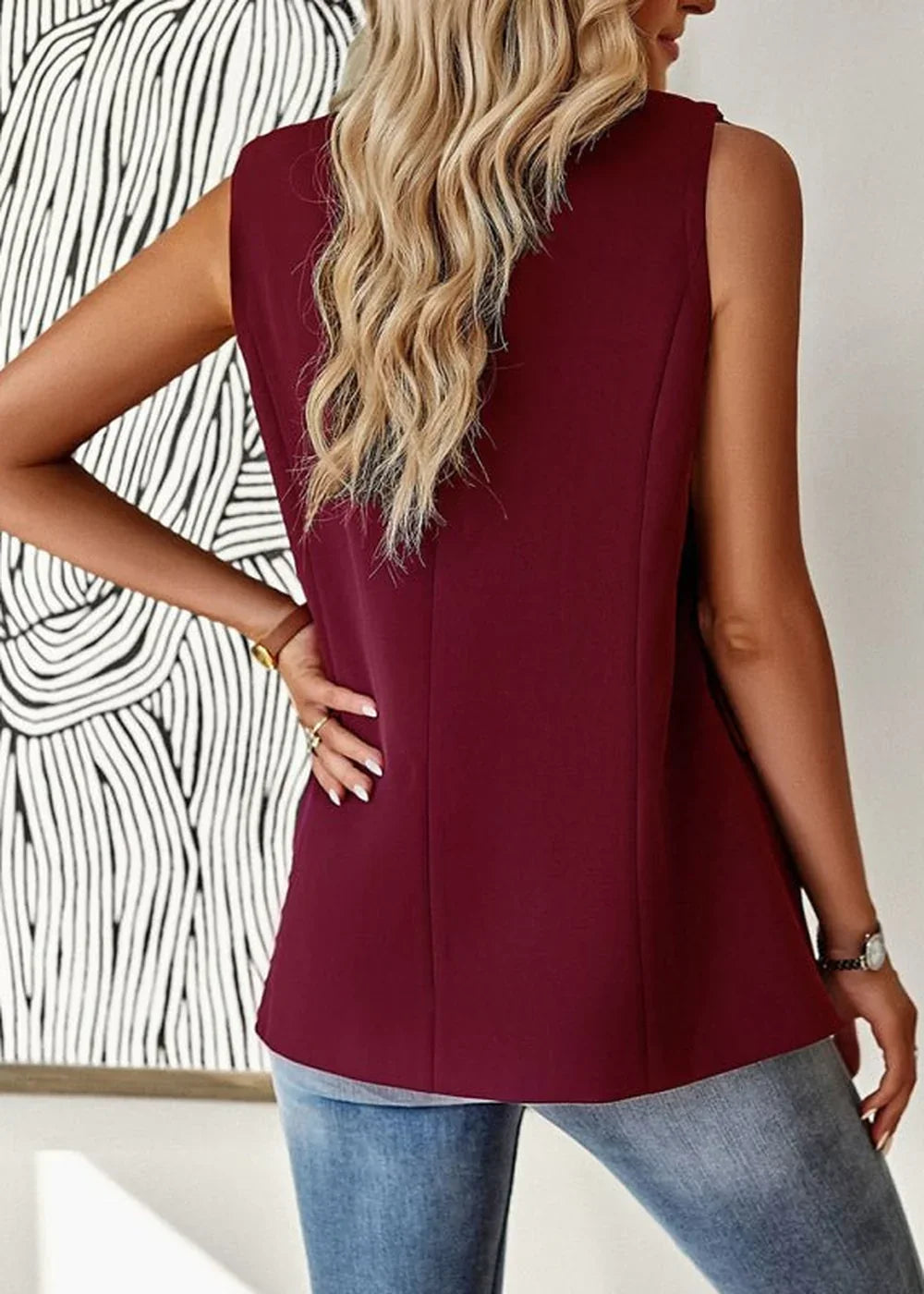 Back view of a sleeveless burgundy blazer on a model wearing blue jeans.