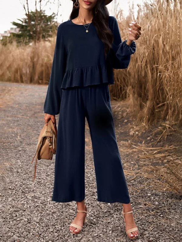 Navy blue linen-blend pant suit with ruffled top and wide-leg pants, worn by a model with tan sandals and a brown bag.