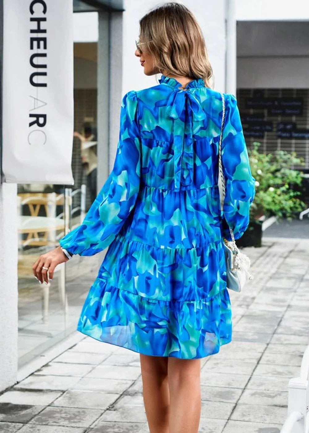 Blue and teal floral print tiered mini dress with a tie-neck and long sleeves.