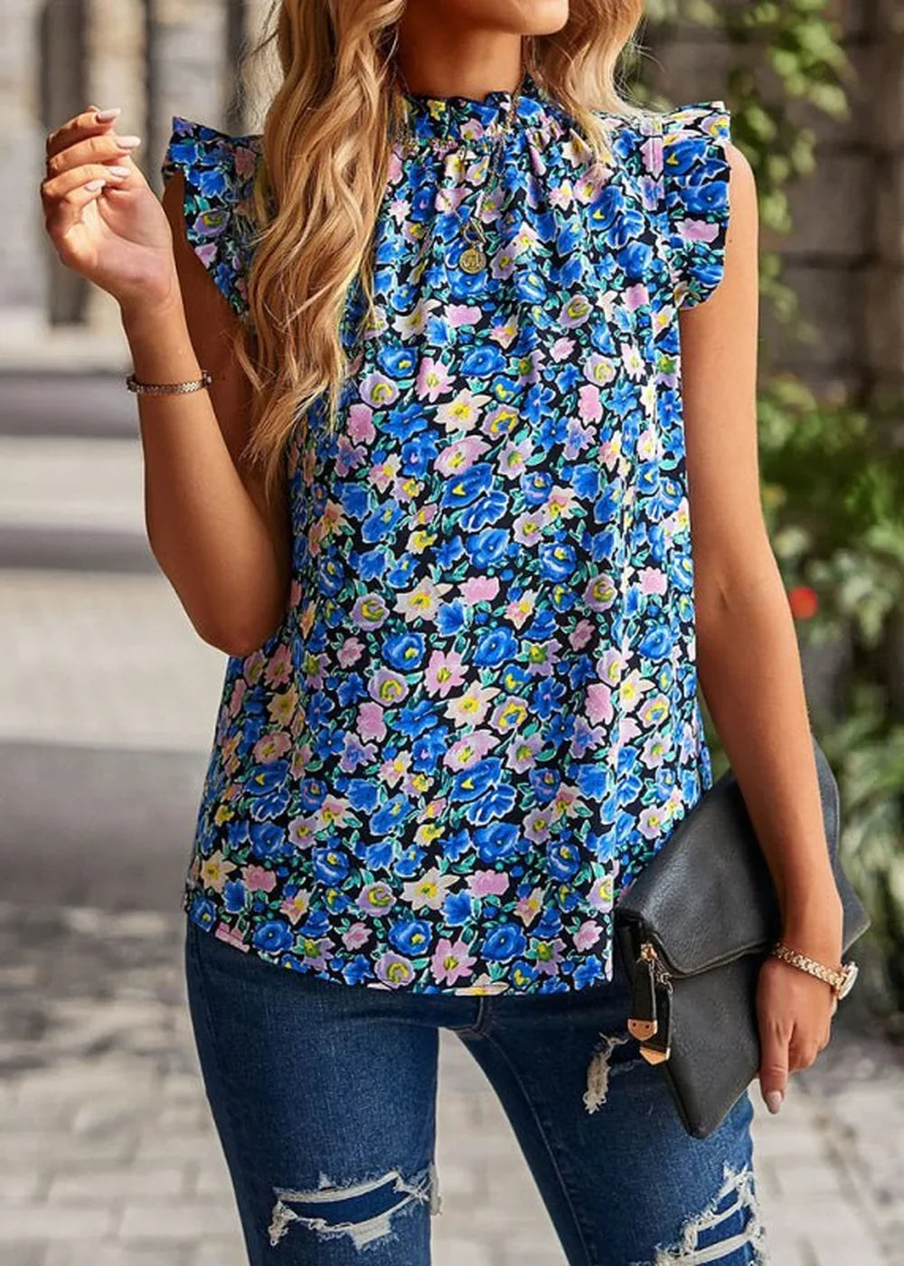 Woman in a blue floral print sleeveless top with ruffled sleeves and ripped jeans, holding a black clutch.