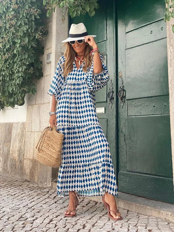 Woman in a navy and white diamond print maxi dress, white hat, and straw bag.