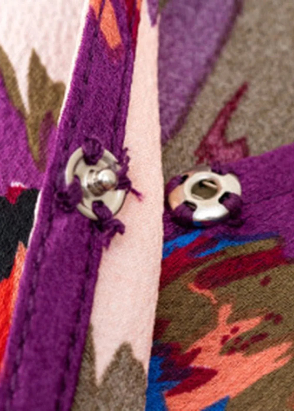 Close-up of a dress with a vibrant floral print in purple, pink, and brown, featuring snap closures.