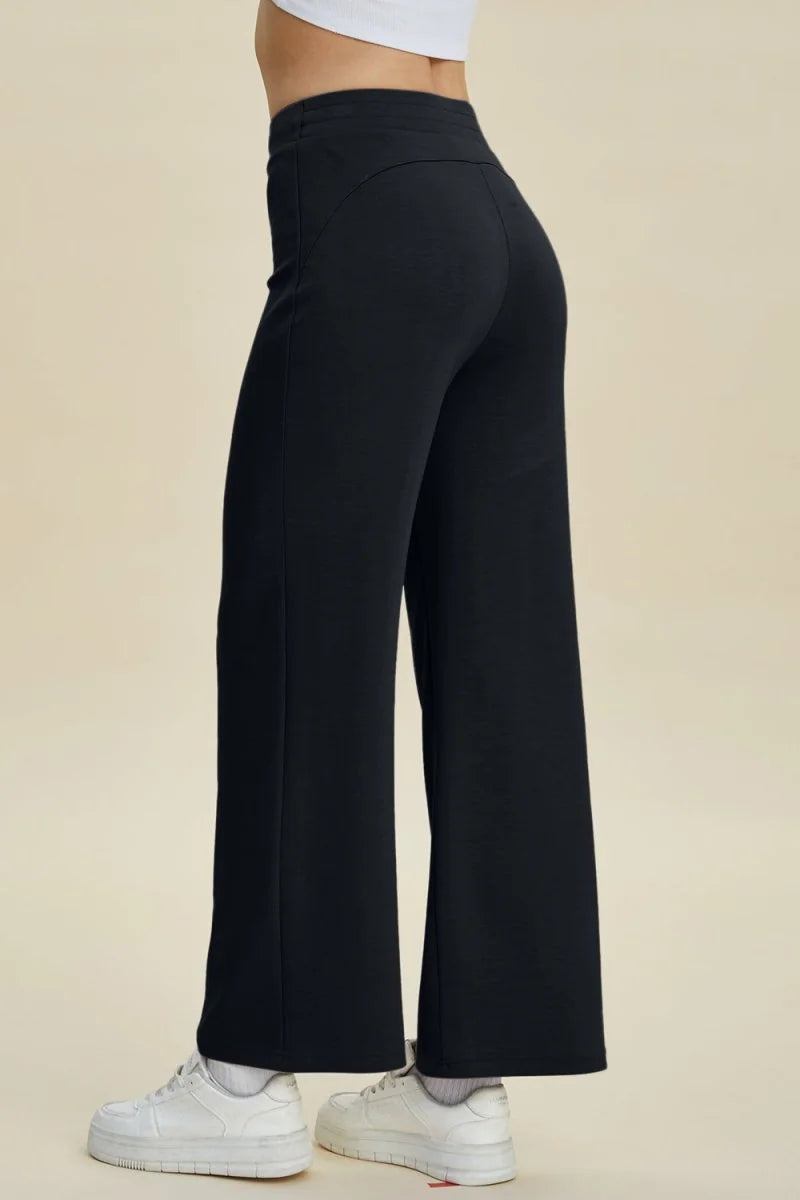 Black wide-leg pants with a regular fit, seen from the side on a model wearing white sneakers.