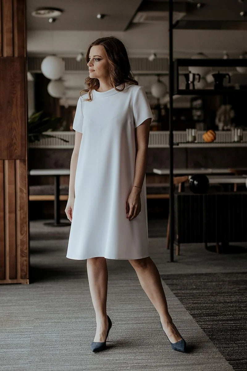 Woman in a loose-fit, short-sleeve white A-line dress and dark heels.
