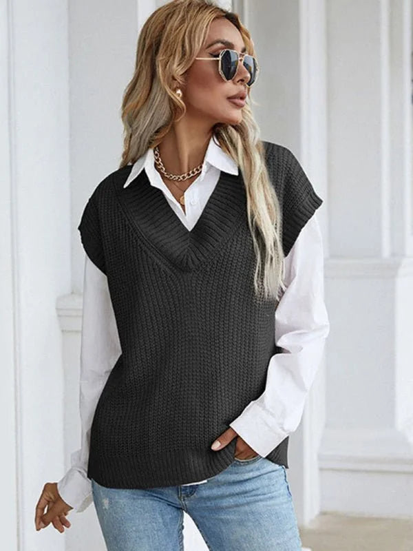 Woman wearing a charcoal gray v-neck knit vest over a white button-down shirt and blue jeans.