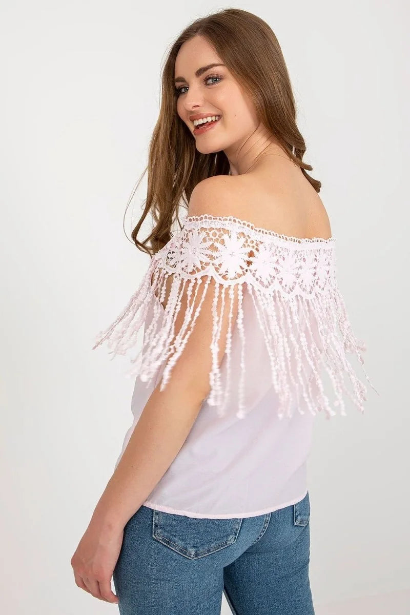 Light pink off-the-shoulder top with delicate lace and fringe detail, paired with blue denim jeans on a model.