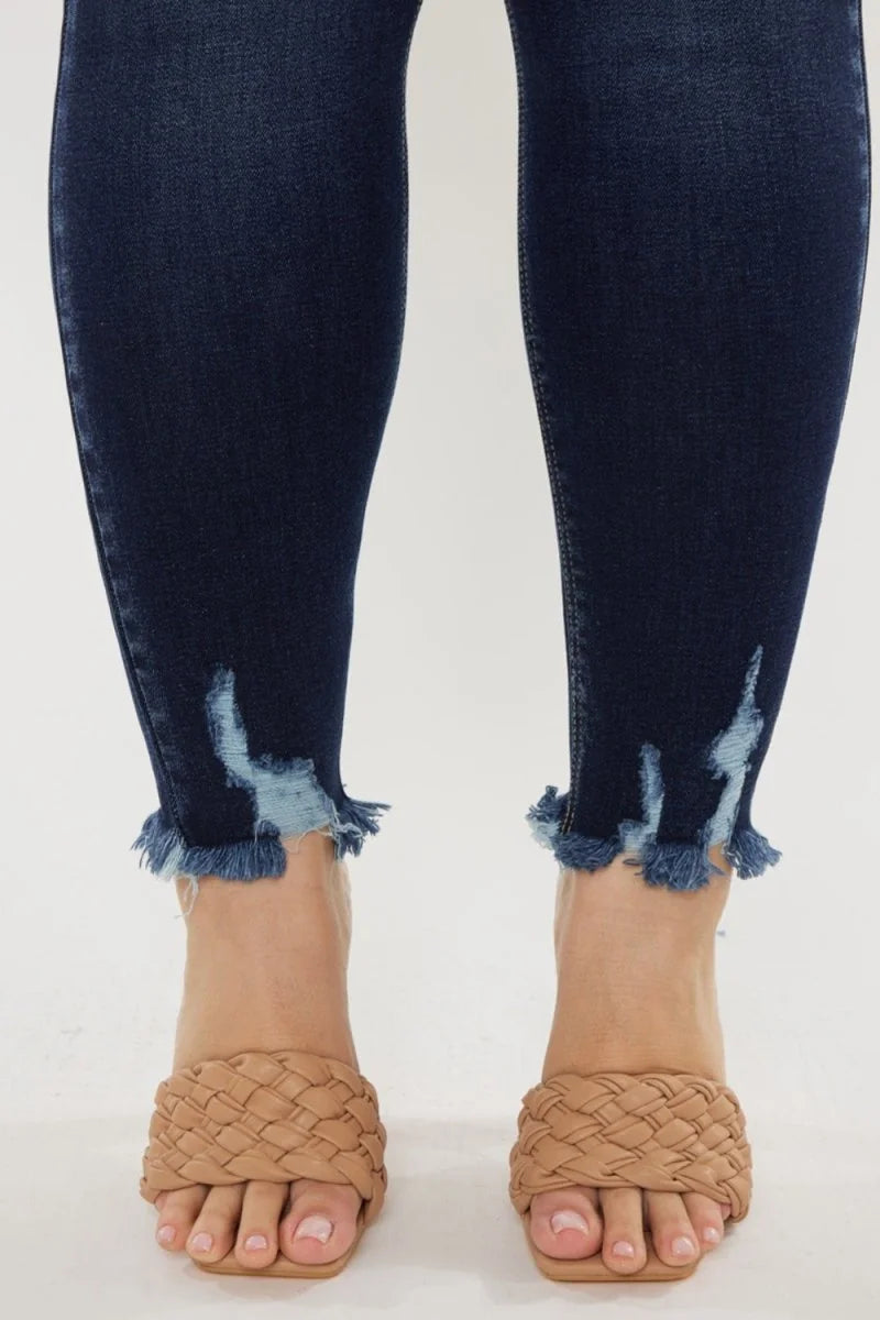 Close-up of dark wash denim jeans with frayed hem detail and woven tan slides.
