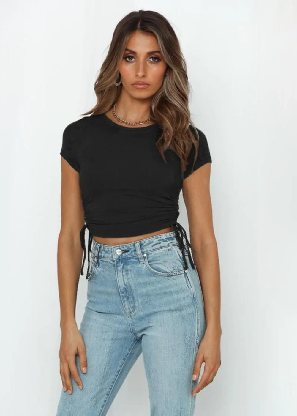 Black ruched crop top with drawstring sides and light wash denim jeans on a model.