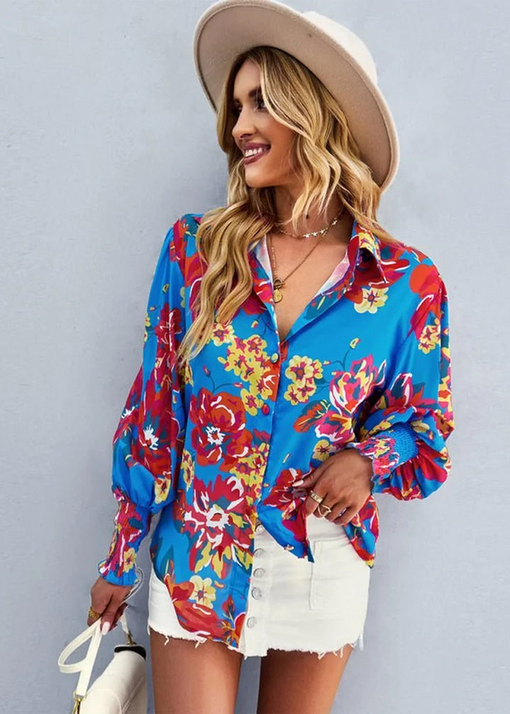 Blue long-sleeved shirt with vibrant floral print, featuring a button-down front and white denim shorts.