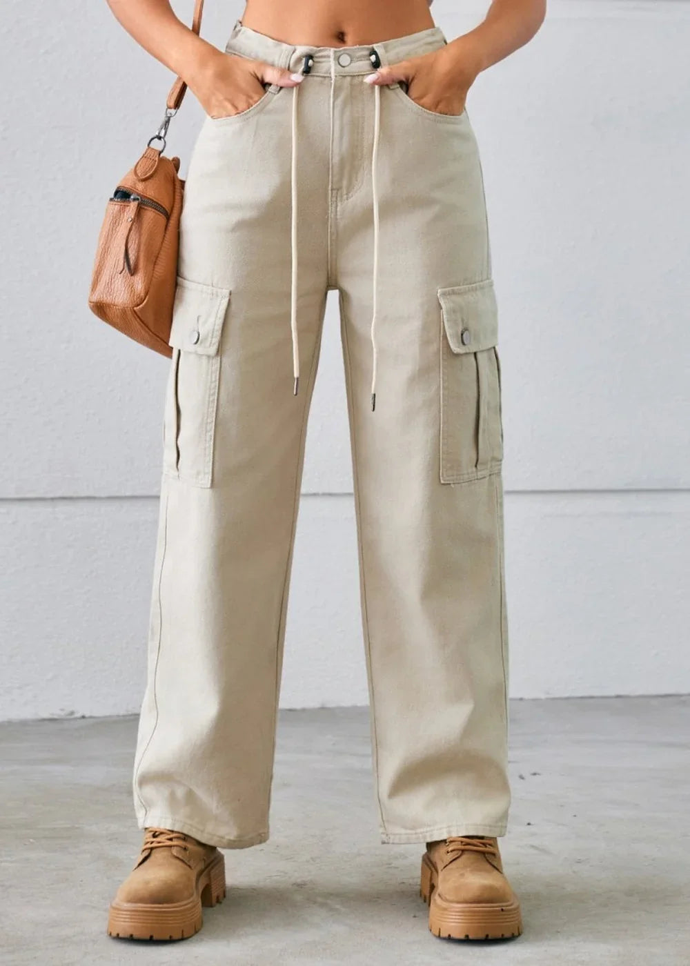 Light beige cargo pants with drawstring waist and large side pockets, worn by a model with brown chunky shoes.