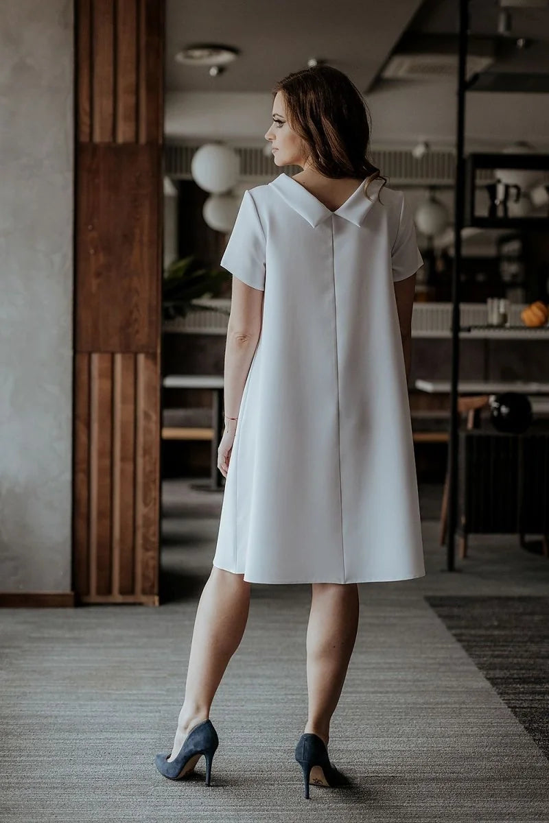 Loose fit white short-sleeve dress with a collar, worn with dark blue heels.