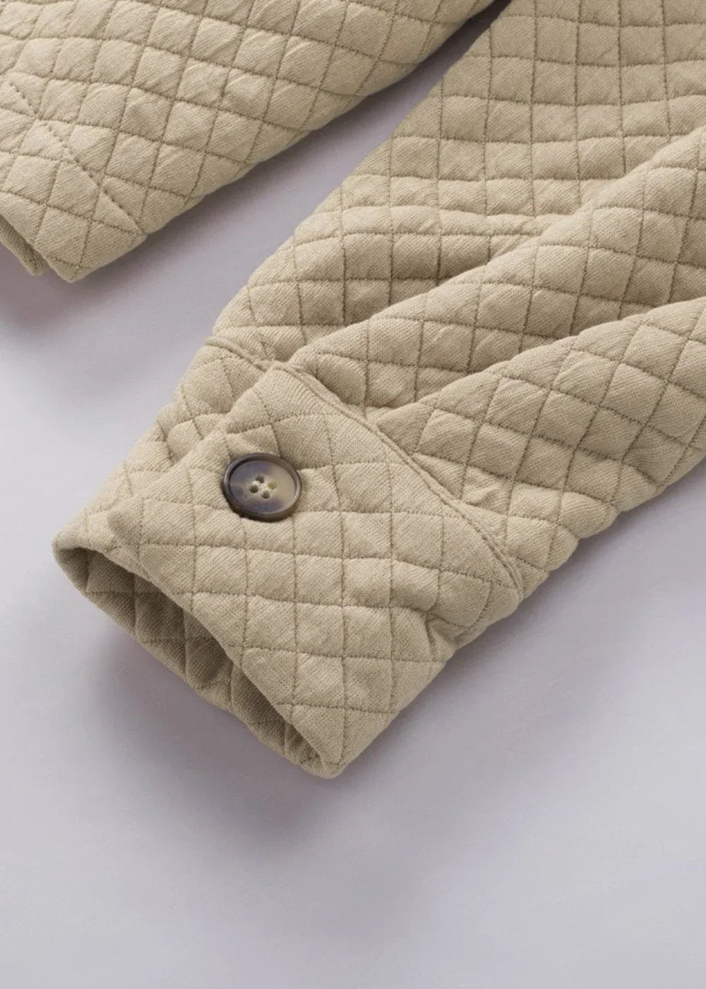 Close-up of a tan quilted jacket sleeve with a brown button and diamond pattern texture.