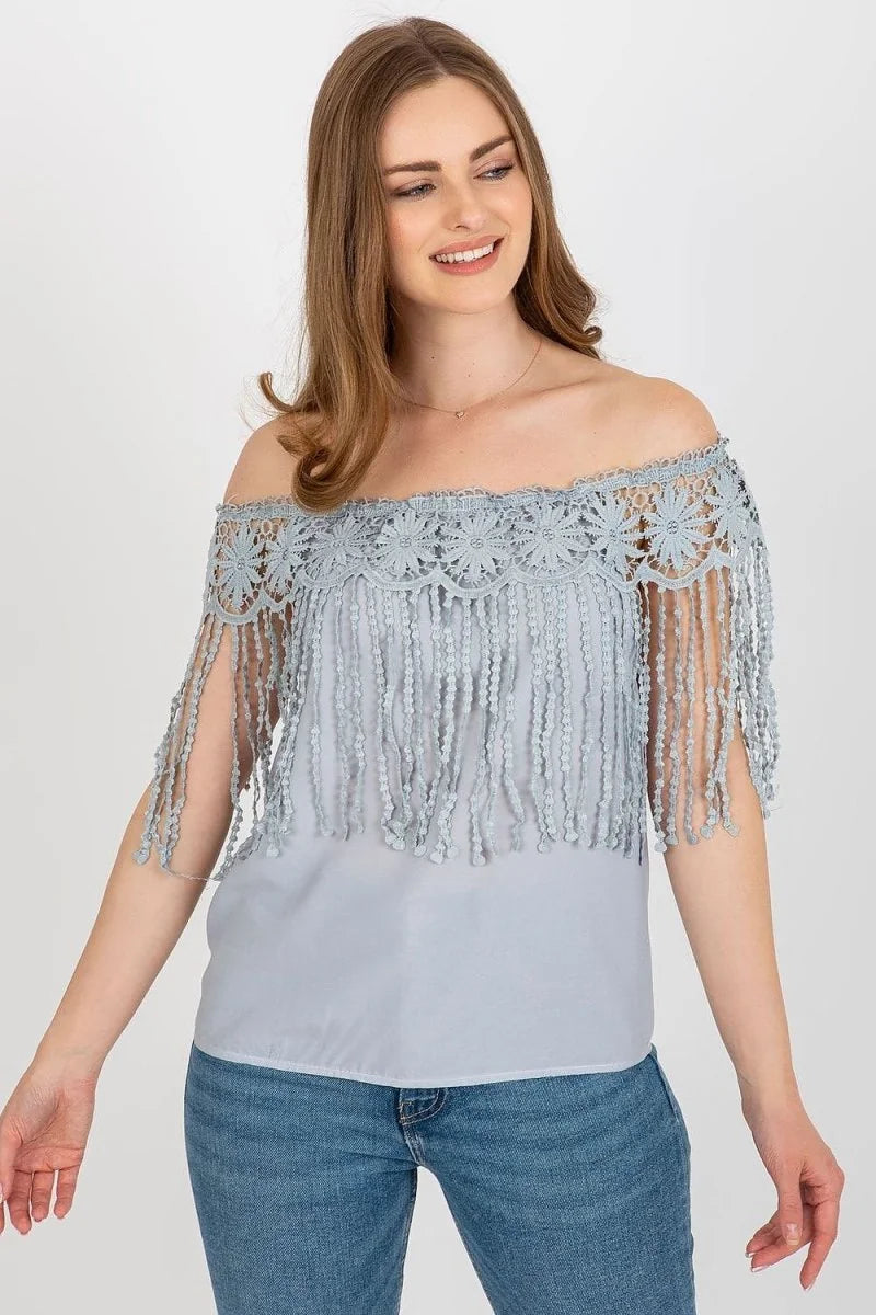 Light blue off-the-shoulder top with intricate lace and fringe detail, paired with blue jeans.
