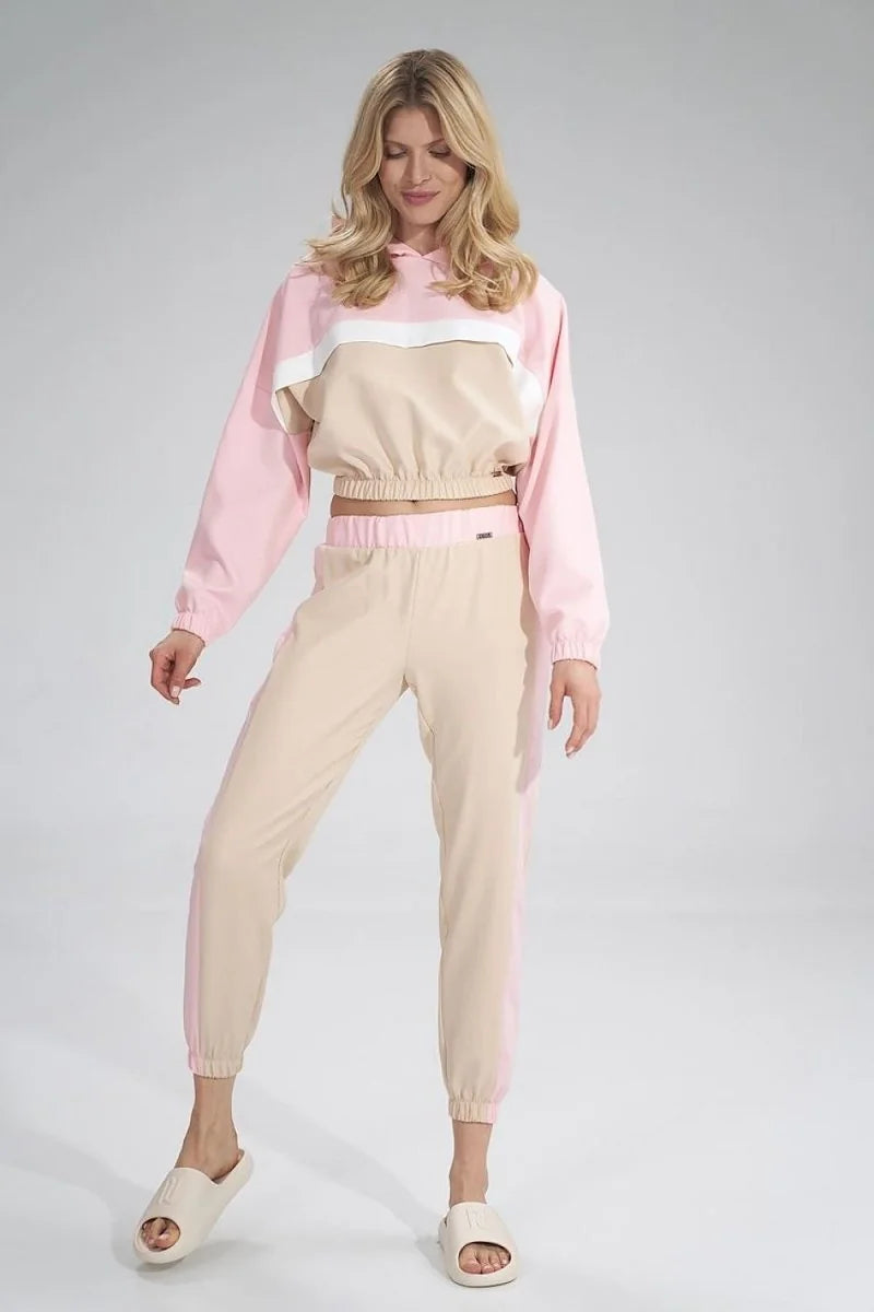 A woman wears a pink and beige cropped hoodie with white accents and matching striped pants.