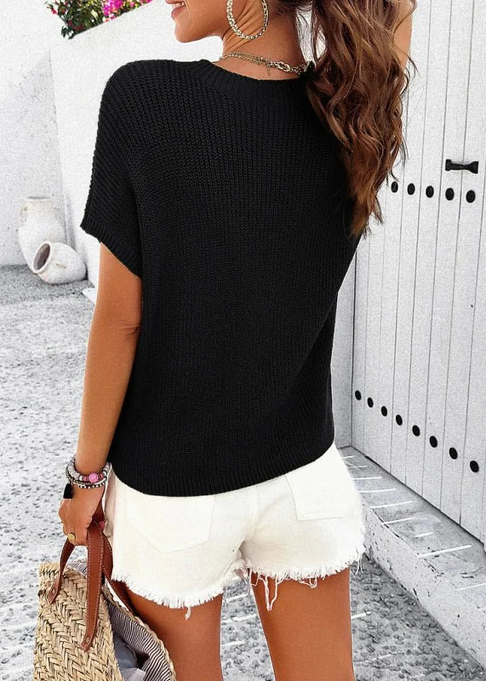 Black knit short-sleeve top with white frayed denim shorts, on model.