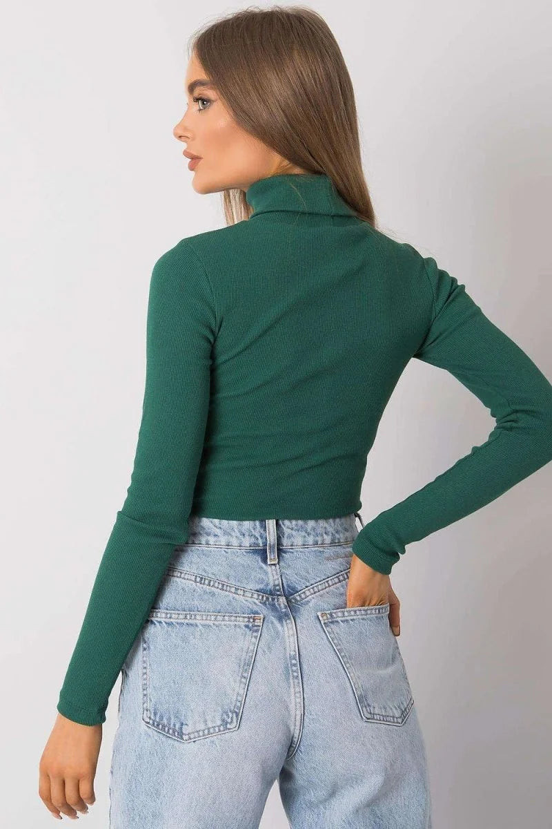 Fitted green ribbed turtleneck crop top with long sleeves, paired with light wash denim jeans.