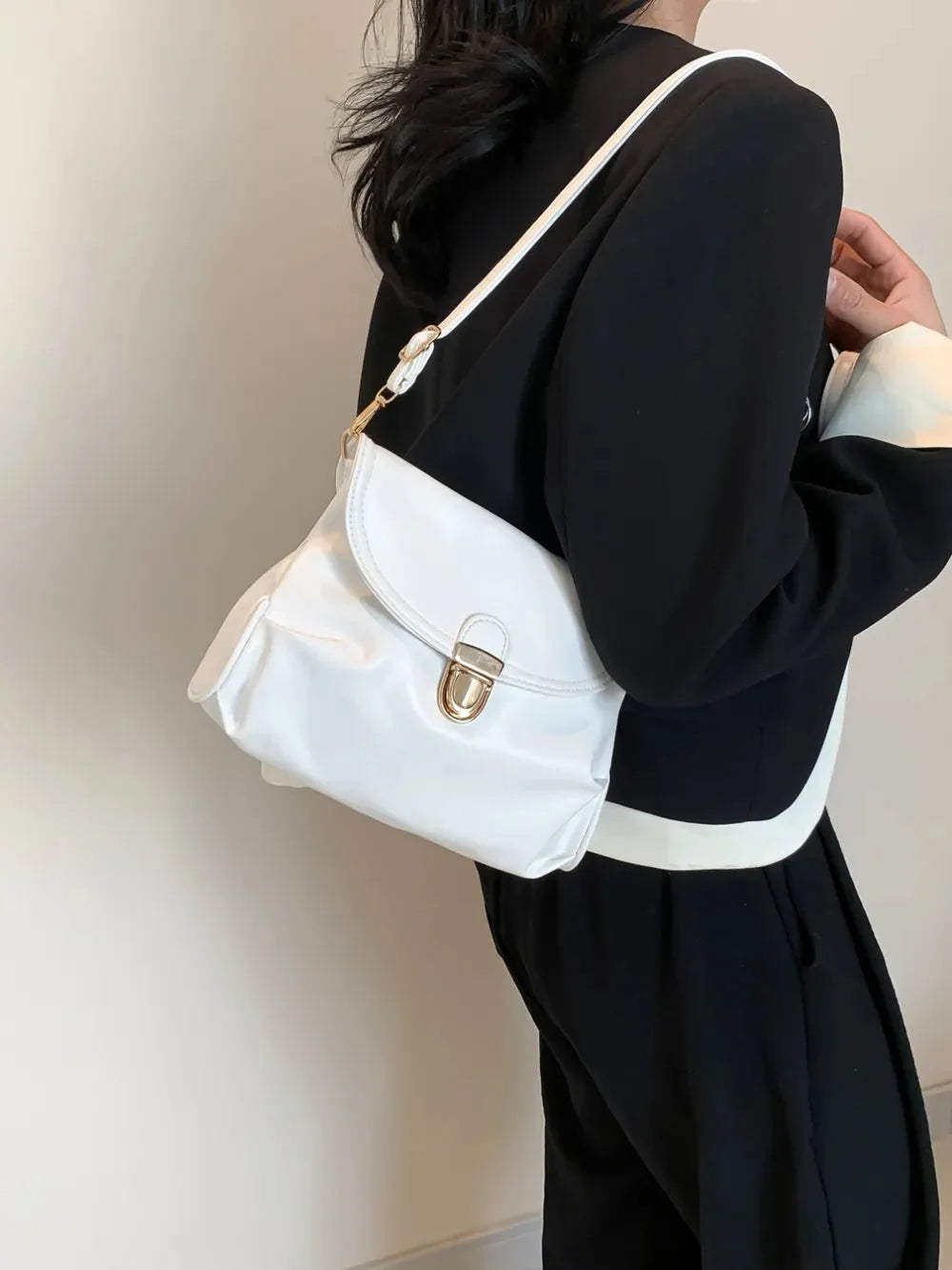 White leather shoulder bag with gold hardware, worn with a black and white jacket.