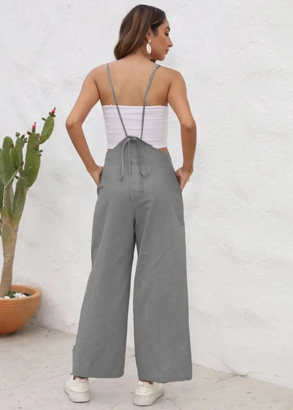 Back view of gray wide-leg overalls with a tie-back detail, worn by a model with white sneakers.