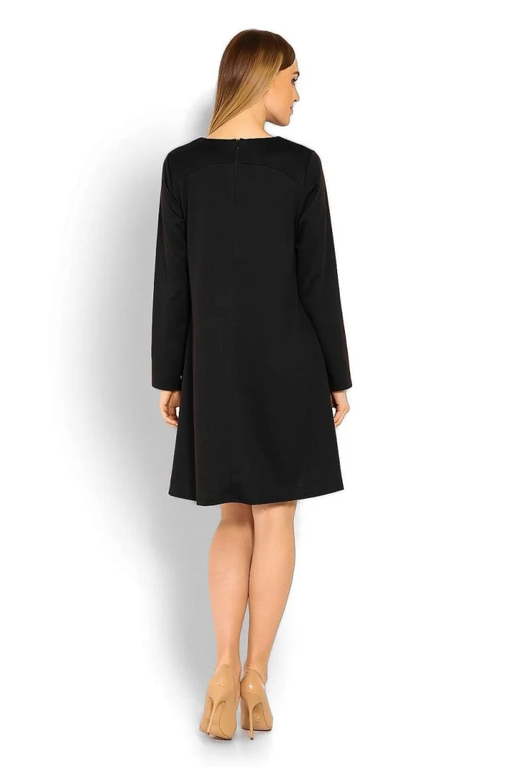 Back view of a black, loose-fit, long-sleeved A-line dress on a model, paired with nude heels.